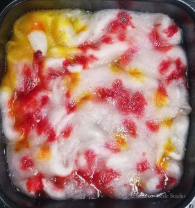 Red, yellow, and neon pink food coloring dropped onto white roving.